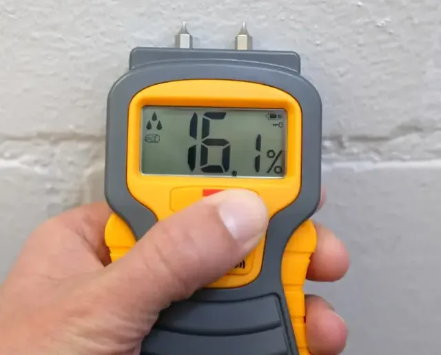Handheld moisture meter checking a textured interior wall