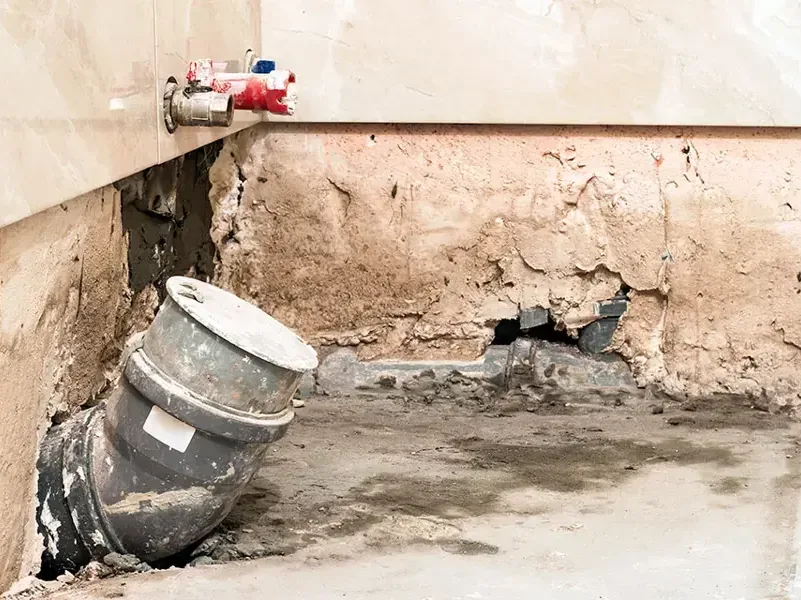 Wall opened at the base to expose a drain pipe behind a leak