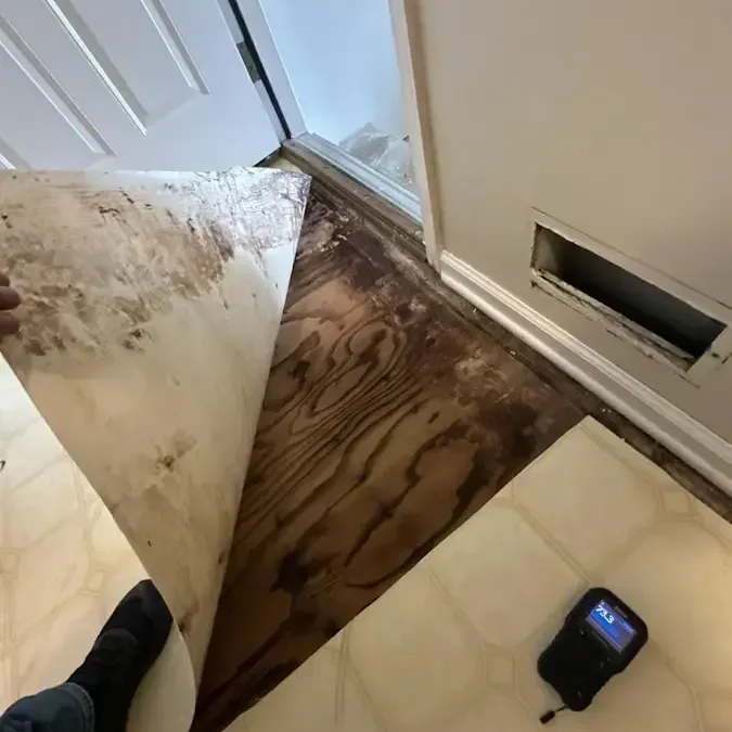 Water-damaged flooring pulled back with a moisture meter beside it