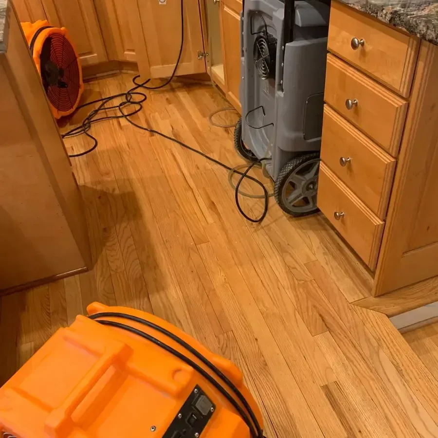 Air mover and dehumidifier drying a hardwood kitchen floor after a leak