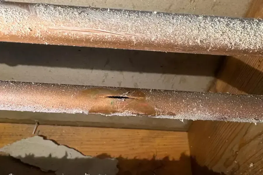 Frost-covered copper pipes in a joist bay, one split open by a hard freeze
